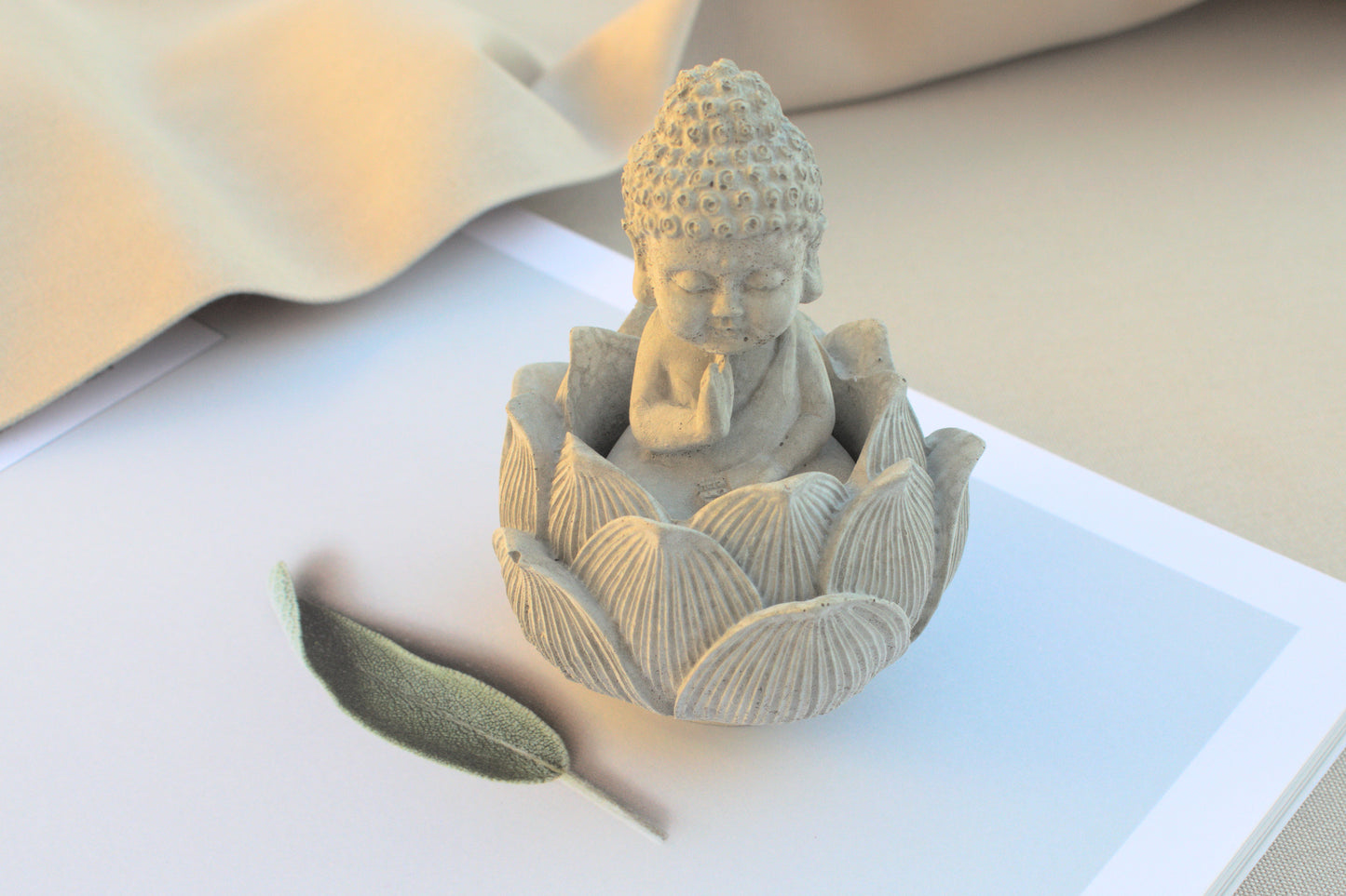 Kleiner Buddha mit Lotusblüte aus grauem Beton für Ruhe beim Yoga
