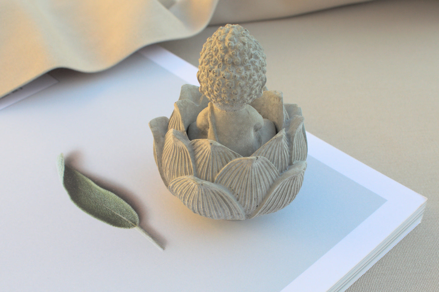 Kleiner Buddha mit Lotusblüte aus grauem Beton für Ruhe beim Yoga